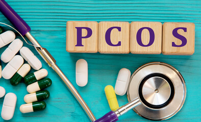 PCOS - acronym on wooden cubes on a blue background with a stethoscope and tablets