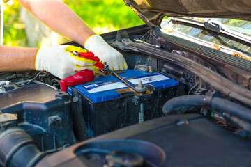 Under the open hood of a car, an auto mechanic unscrews the car battery holder in order to repair or replace it. Transport service