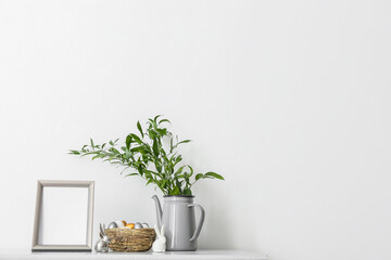 Blank photo frame, nest with Easter eggs and different plant branches on table near light wall