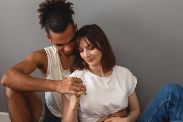 A couple, a guy and a girl are sitting at home on the floor against a gray wall