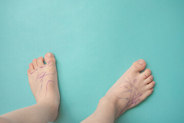 The feet of young boy streaked with felt-tip pens on a light blue background with empty copy space.