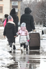 a family of four with a dog leaves the city for a trip and walks along the road with a large suitcase in the winter season through the snow