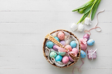 Basket with painted Easter eggs, tulip flowers and bunny on light wooden background