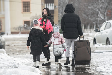 a family of four with a dog leaves the city for a trip and walks along the road with a large suitcase in the winter season through the snow