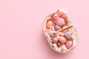 Basket with painted Easter eggs and bunny on pink background