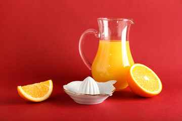 Fototapeta na wymiar Ceramic juicer, jug of juice and orange on red background