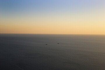 Two ships sailing towards each other in the middle of the sea against the backdrop of a picturesque horizon with a gradient sky at sunset