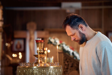 a bearded man in a headscarf prays in an Orthodox church and puts candles in front of icons