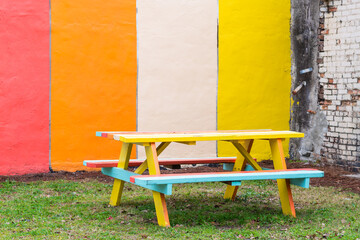 Colorful picnic table with benches on the grass against a painted wall