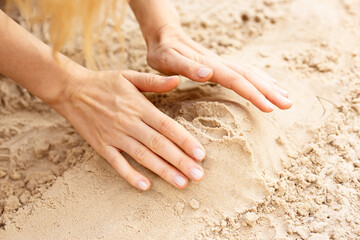 close up photo of woman hands sculpting vagina from white sand