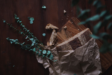 Flat lay shot of rustic brown malted loaf of bread. Cut on a wooden chopping board. Bread crumbs and eucalyptus leaves scattered in shot. Copy space available