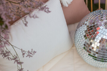 Shiny disco ball on a white cushion and purple plants on the side