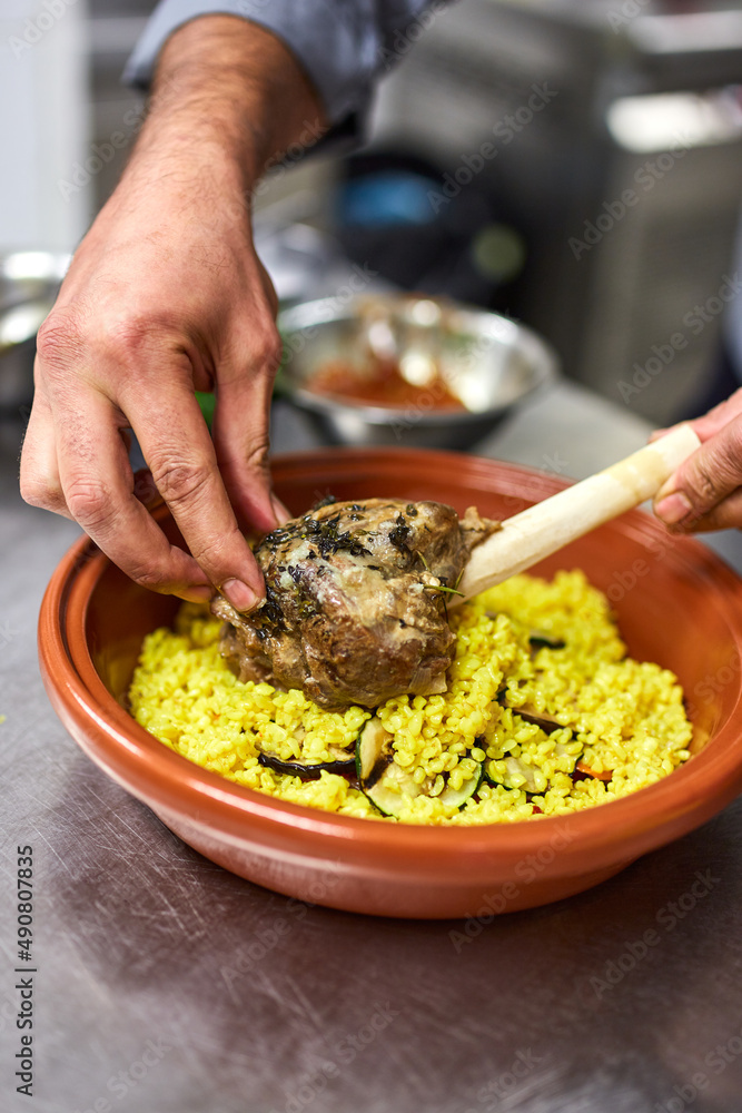 Poster Closeup vertical shot of a chef holding a lamb meat with yellow rice on an orange ceramic plate