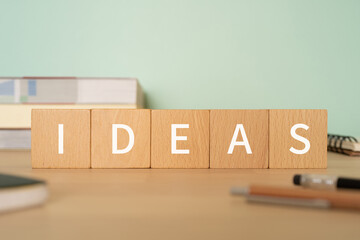 アイデアのイメージ｜「IDEAS」と書かれた積み木、参考書、ノート、ペン