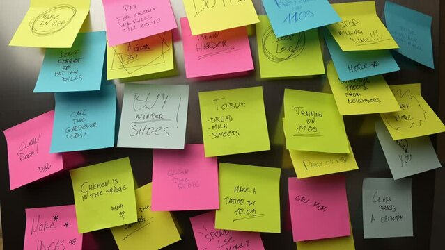 A woman puts a sticker with a to-do list and a shopping list on the refrigerator, the camera pulls back and shows a huge number of stickers and reminders on the refrigerator door. Memory and time