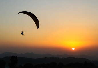 Beautiful shot of a human paragliding during sunset at Bir, Himachal Pradesh, India - obrazy, fototapety, plakaty