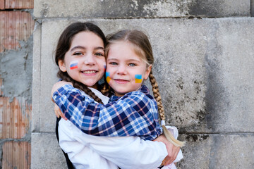 Portrait of two little girls embracing with Russian and Ukrainian flags on the faces. Concept of...