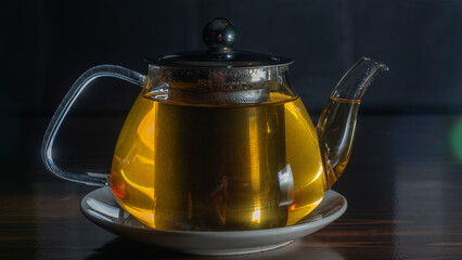 Glass teapot with tea on dark background. Green tea and teapot on wooden table. Advertising...