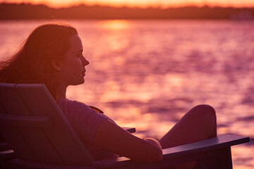 Young woman sits on the beach and enjoys the sunset over the sea