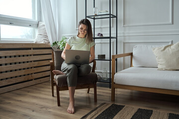 Young woman using laptop, typing, sitting in a chair, remote work, work at home