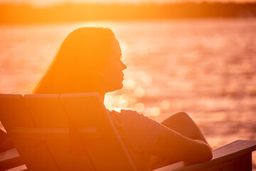 Young woman sits on the beach and enjoys the sunset over the sea