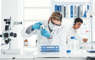 Cropped shot of an attractive young female scientist transferring a liquid sample from a dropper into test tubes in a laboratory with her colleague in the background