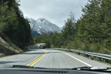 Viaje en carretera con paisaje de montaña nevada y bosque tupido.