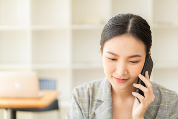Asian businesswomen Smile and enjoy working with smartphones and laptops at home with beautiful blur background business idea.