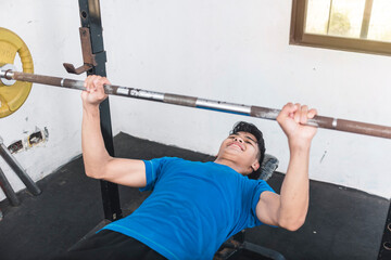A young man struggles to lift a barbell to heavy for his strength level. Added to much weight...