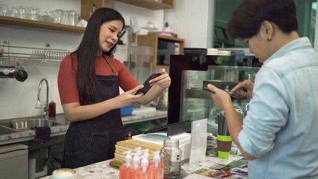 Coffee shop owners accept payments from customers by paying via smartphone, scanning QR Codes instead of cash as contactless payments, and serving coffee to customers in coffee shop concept.