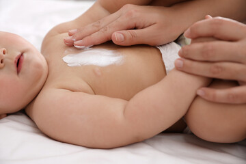 Mother applying moisturizing cream onto her little baby's skin on bed, closeup