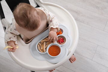 Little baby eating food in high chair indoors, top view