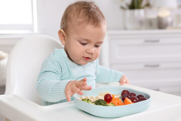 Cute little baby eating food in high chair at home