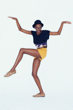 Shes hip and happening. Studio shot of a young ethnic hipster balancing on one leg with her arms raised.
