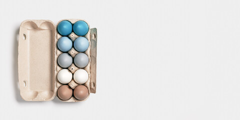 Obraz na płótnie Canvas Colorful Easter eggs in carton packing, blue, beige, white neutral colors, festive chicken egg in paper container on lihgt grey colored background. Minimal style aesthetic composition