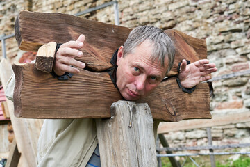 Man in wooden stocks from medieval times for use with prisoners, criminals - obrazy, fototapety, plakaty