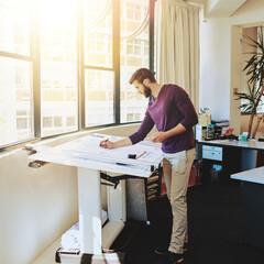 Making some adjustments. Full length shot of a young architect working on his drafting table.