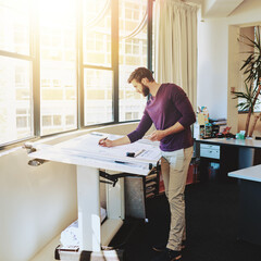 Making some adjustments. Full length shot of a young architect working on his drafting table.