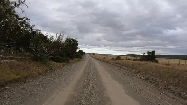 Rural road. Countryside scene. Point of view of a vehicle speeding across the dirt road in the ranch. We can see the backwoods and yellow meadow in autumn.