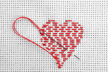 Canvas with embroidered heart and needle as background, top view