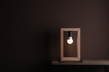 Wooden table with lamp near brown wall in room, space for text