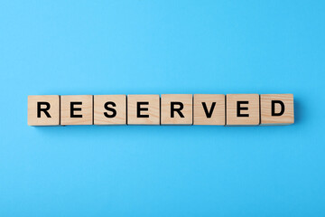 Wooden cubes with word Reserved on light blue background, flat lay