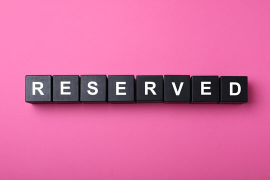 Black cubes with word Reserved on pink background, flat lay