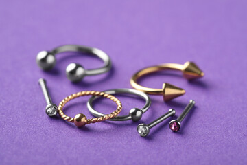 Stylish piercing jewelry on violet background, closeup