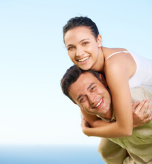 Fototapeta premium Enjoying their holiday. A young man giving his girlfriend a piggyback with the ocean in the background.