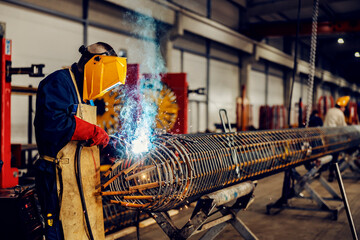 Metallurgy worker working with welding machine on metal framework in factory.