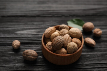Bowl with nutmeg seeds on black wooden table, closeup