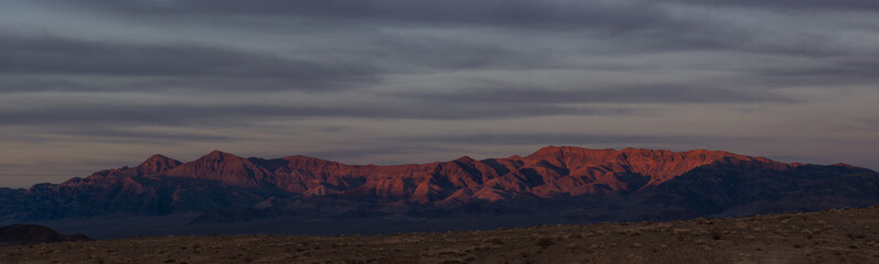 Desert landscape of the Nopah range in Inyo County, California. This panoramic image was taken at dusk and shows a sky with clouds and muted colors.