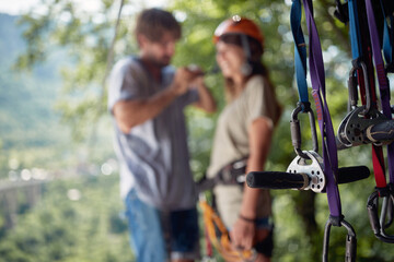 Selective focus on protection gear with blurred background of couple. Young attractive couple in casual clothing preparing for zip line adventure in forest.  Holiday, adventure, extreme sport concept.