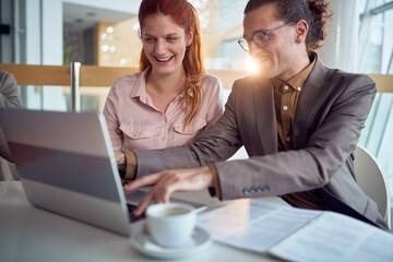 A young businessman is having a good time with female colleague while they enjoying a laptop content in the company building together. Business, people, company